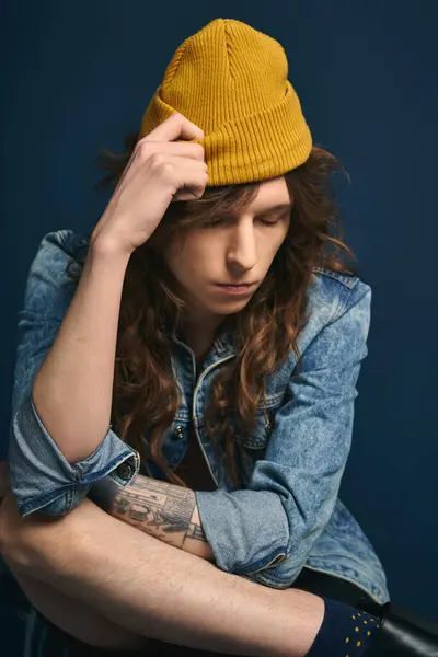 Un bel giovane uomo con i capelli lunghi e un berretto guarda pensieroso mentre indossa una giacca di jeans. — Foto stock