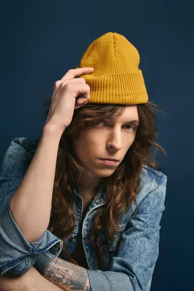 A fashionable young man showcases his unique style with confidence against a deep blue backdrop. — Stock Photo