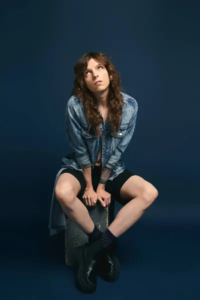 Handsome young man seated on a stool showcases trendy denim attire with a relaxed yet chic vibe. — Stock Photo