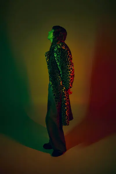 A young, handsome man stands stylishly in vivid lighting while modeling chic attire. — Stock Photo