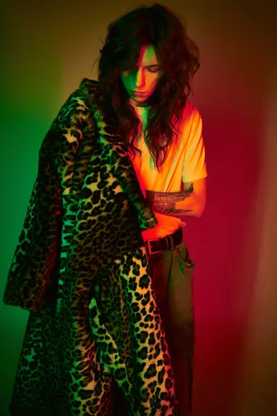A stylish young man stands confidently, draped in a leopard print coat against a striking backdrop. — Stock Photo