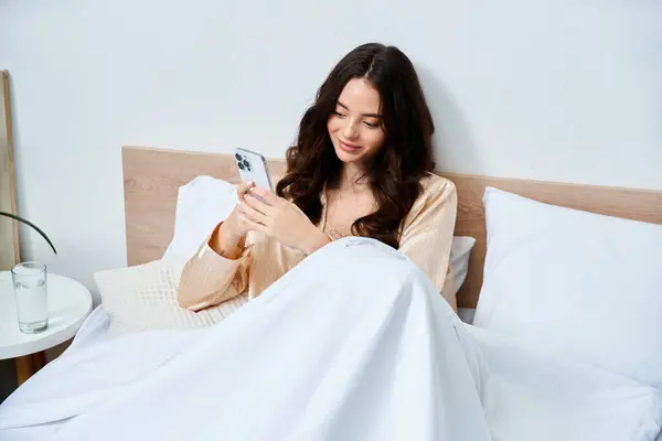 A beautiful young woman smiles while scrolling through her smartphone in a cozy bed. — Stock Photo
