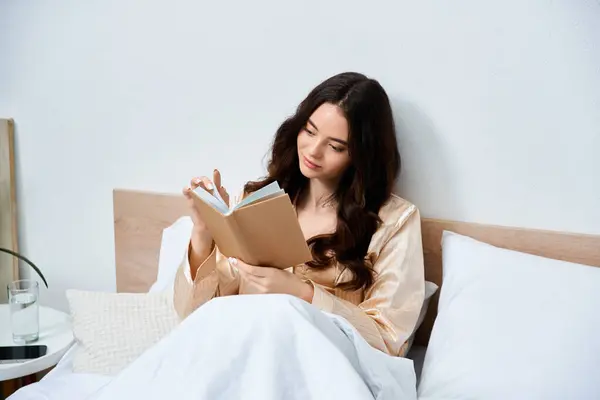 A young woman enjoys a quiet morning, reading a book while nestled in bed. — Stock Photo