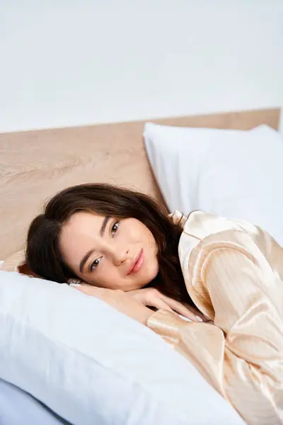 A lovely young woman smiles while lying on her side, surrounded by soft pillows. — Stock Photo