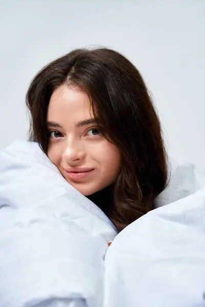 A beautiful young woman smiles playfully while wrapped in cozy blankets, exuding warmth and comfort. — Stock Photo