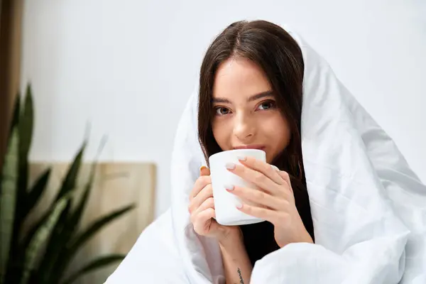 Young woman enjoys a hot beverage while wrapped in a blanket, savoring a tranquil morning ambiance. — Stock Photo