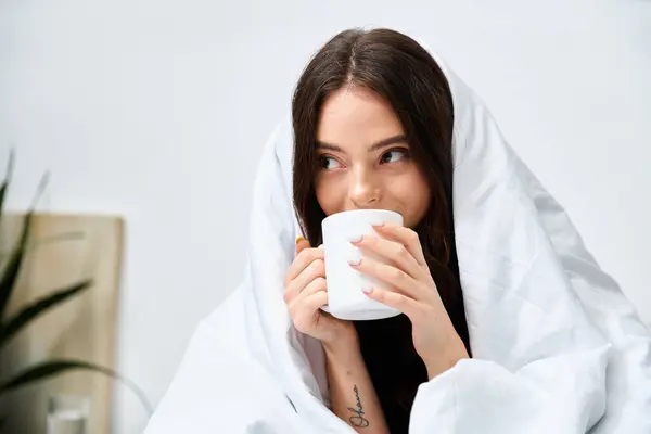 A young woman wrapped in a blanket savors a warm drink, radiating comfort and joy indoors. — Stock Photo