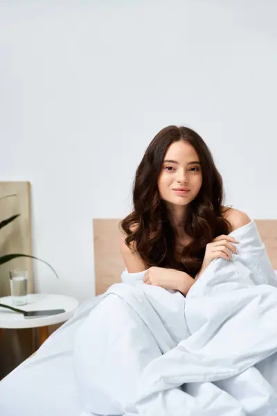 Charming young woman sits comfortably in a cozy bed, enjoying a tranquil morning vibe. — Stock Photo