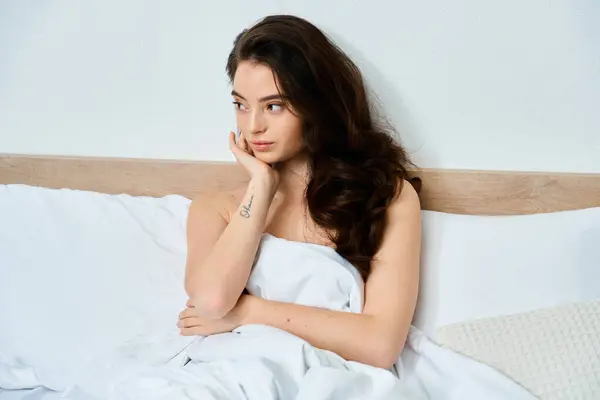 A young woman gazes out with a pensive expression while resting on a bed. — Stock Photo