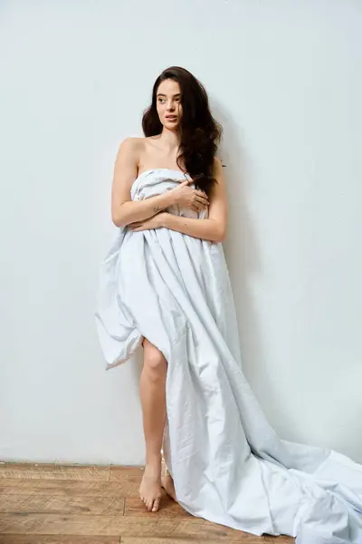A beautiful young woman poses elegantly in soft light, wrapped in flowing fabric and exuding charm. — Stock Photo