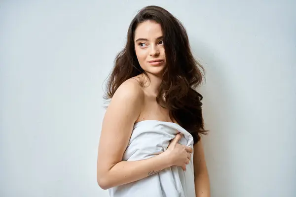 A beautiful young woman stands elegantly against a pale backdrop, exuding confidence and allure. — Stock Photo