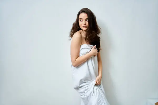 A lovely young woman elegantly wraps herself in gentle fabric while striking a charming pose. — Stock Photo