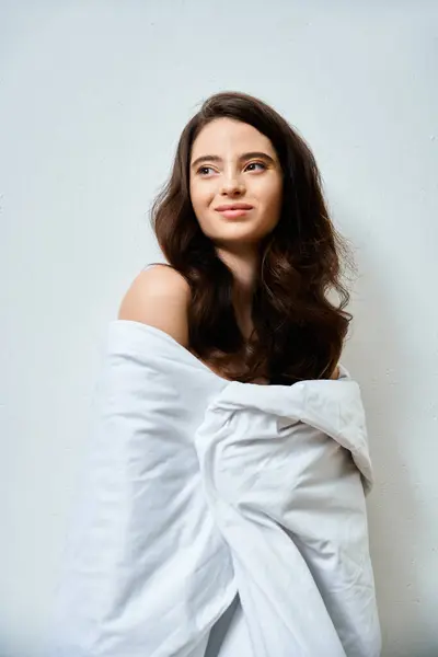 Une jeune femme aux cheveux fluides sourit doucement, enveloppée dans un tissu blanc douillet, rayonnant d'élégance. — Photo de stock