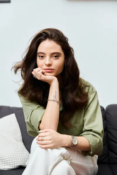 A beautiful young woman rests her chin on her hand, lost in thought while seated comfortably. — Stock Photo