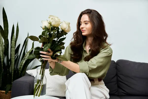 A beautiful young woman smiles gently while arranging fresh white roses in a glass vase at home. — Stock Photo