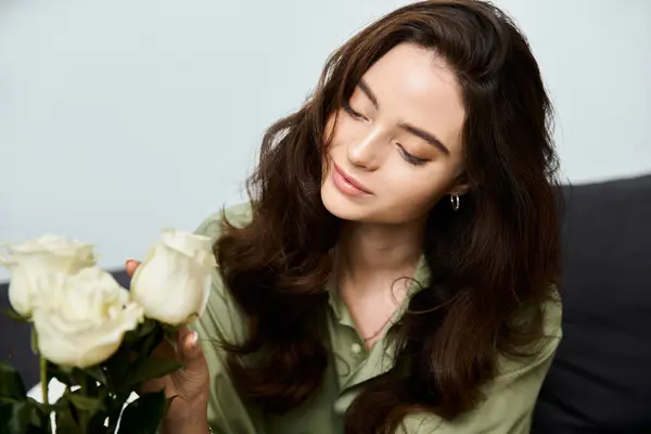 A beautiful young woman admires white roses while sitting peacefully in a stylish living room. — Stock Photo
