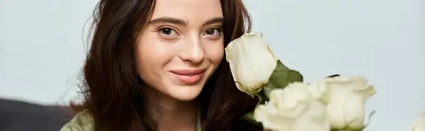 A joyful young woman with dark hair enjoys white roses, radiating warmth in a peaceful space. — Stock Photo