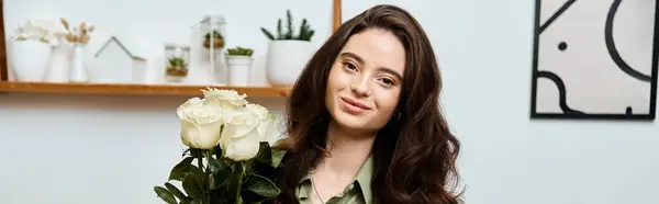 A beautiful young woman holds a bouquet of fresh white roses, exuding joy in a stylish room. — Stock Photo