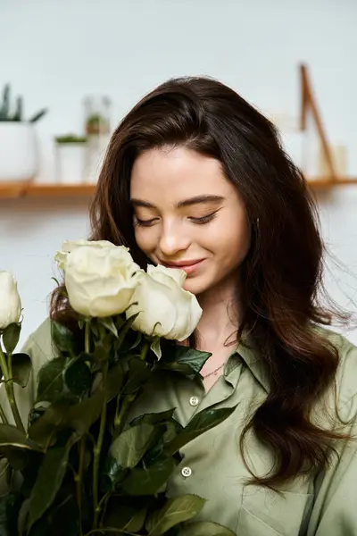 A beautiful young woman smiles softly while holding a bouquet of white roses indoors, radiating joy. — Stock Photo