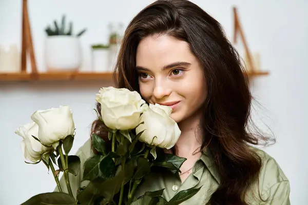 A lovely young woman enjoys the beauty of white roses while smiling gently in her home. — Stock Photo
