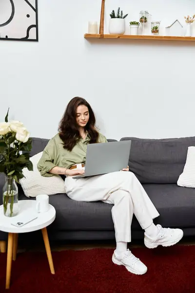 A beautiful young woman is seated comfortably in a stylish living room, focused on her laptop. — Stock Photo