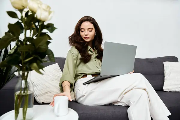 A beautiful young woman in green sips coffee while working on her laptop in style. — Stock Photo