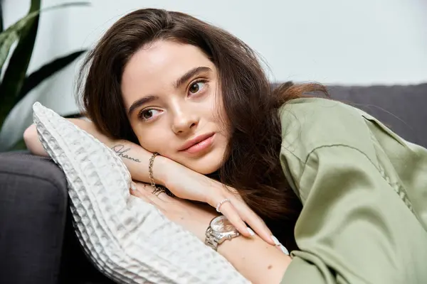 A beautiful young woman lounges on a couch, resting her head on her arm and lost in thought. — Stock Photo