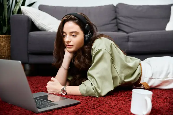 Eine junge Frau entspannt auf einem bunten Teppich, konzentriert auf ihrem Laptop mit Kopfhörern auf dem Kopf.. — Stockfoto