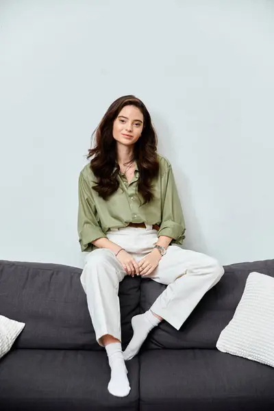 A confident young woman relaxes on a stylish couch in a brightly lit room. — Stock Photo