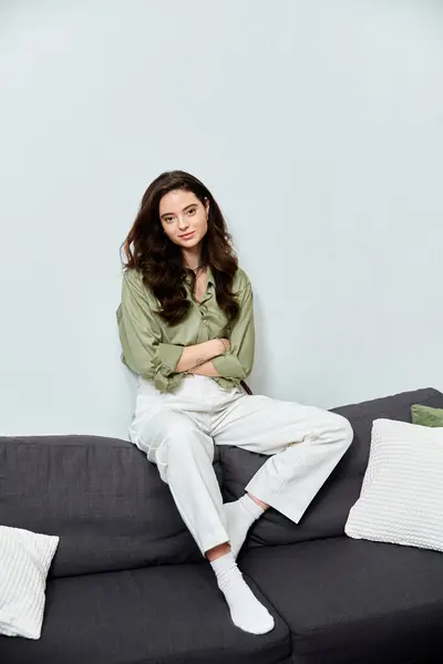 A beautiful young woman sits comfortably on a couch, embracing a relaxed moment in her living space. — Stock Photo