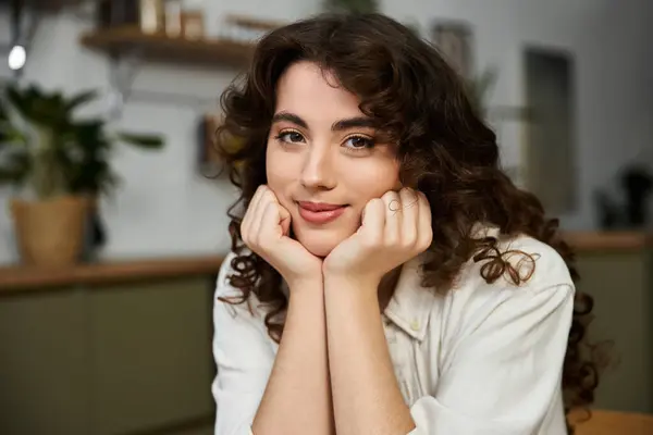 A beautiful young woman rests her chin on her hands, revealing a warm smile while at home. — Stock Photo