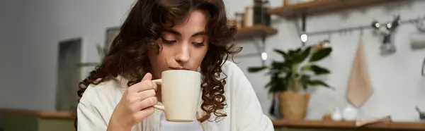 A young woman with curly hair enjoys a warm drink, finding peace in her home. — Stock Photo