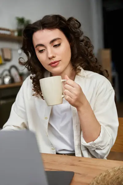 Eine schöne junge Frau sitzt an einem Holztisch, genießt ihren Kaffee und konzentriert ihren Laptop.. — Stockfoto