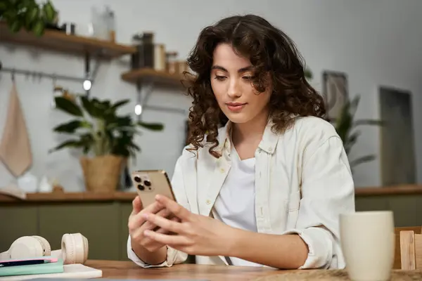A young woman sits at a wooden table, using her smartphone amid greenery at home. — Stock Photo