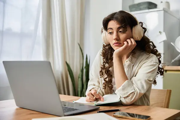 A beautiful young woman sits at her home desk, immersed in thought while listening to music. — Stock Photo
