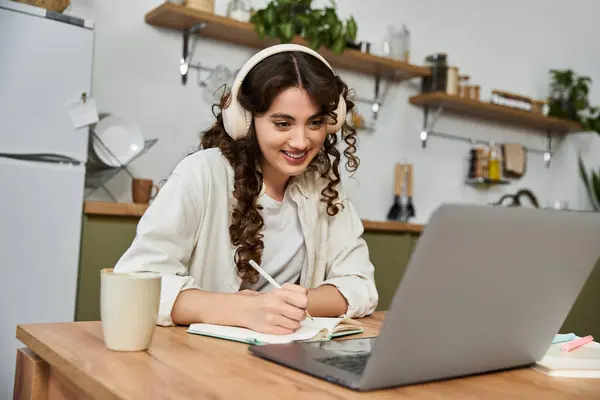 Eine schöne junge Frau lächelt während des Studiums und macht sich Notizen an ihrem gemütlichen Arbeitsplatz zu Hause. — Stockfoto