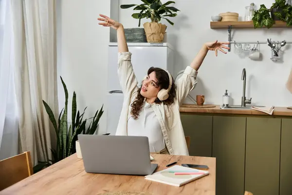 Delighted young woman stretches her arms while engaged in work at her cozy kitchen desk. — Stock Photo