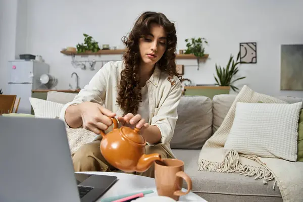 Una joven vierte té en su sofá en casa, disfrutando de un momento de paz. - foto de stock