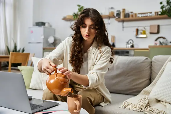Una joven con el pelo rizado vierte té de una olla de barro, disfrutando de su día. - foto de stock