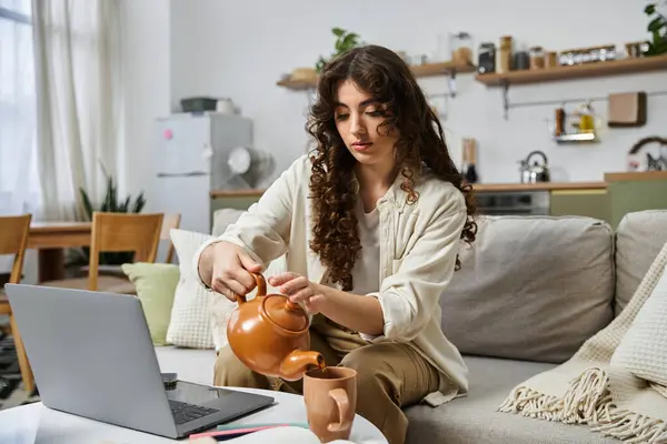 A beautiful young woman relaxes at home, enjoying her favorite beverage and working on her laptop. — Stock Photo