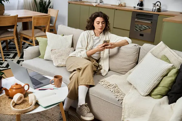 Une jeune femme s'assoit confortablement sur le canapé, appréciant son téléphone et entourée d'un décor maison. — Photo de stock