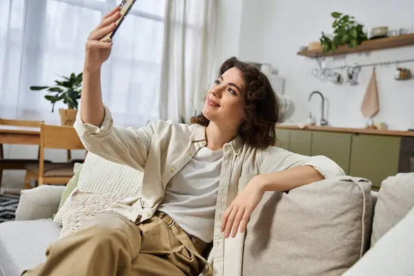 Bright and cheerful young woman relaxes on her couch, capturing a selfie in her beautiful home. — Stock Photo