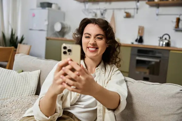 Une jeune femme sourit vivement tout en s'engageant avec son smartphone dans un environnement confortable à la maison. — Photo de stock