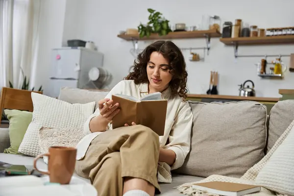 A young woman relaxes on her sofa, absorbed in her favorite book in a cozy home. — Stock Photo