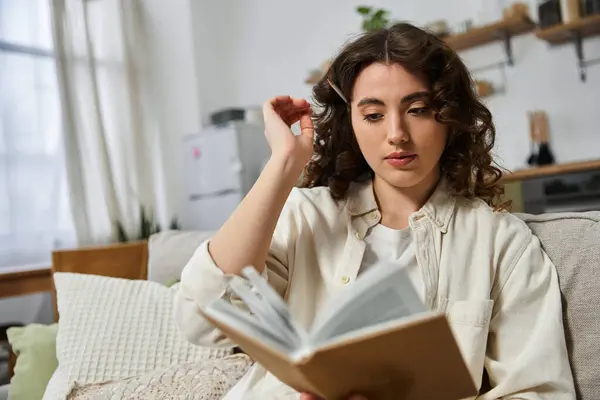 A young woman relaxes at home, deeply engrossed in her book and lost in thought. — Stock Photo