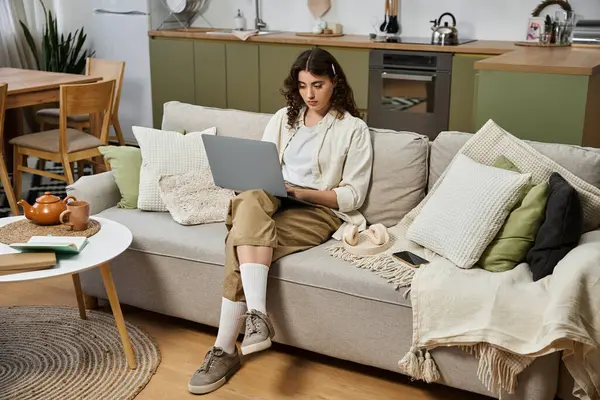 Eine schöne junge Frau entspannt sich auf einem Sofa, während sie sich auf ihren Laptop konzentriert und einen gemütlichen Tag zu Hause genießt. — Stockfoto