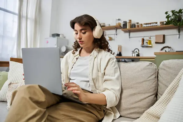 A young woman engages with her laptop, enjoying a moment of creativity in her stylish living room. — Stock Photo