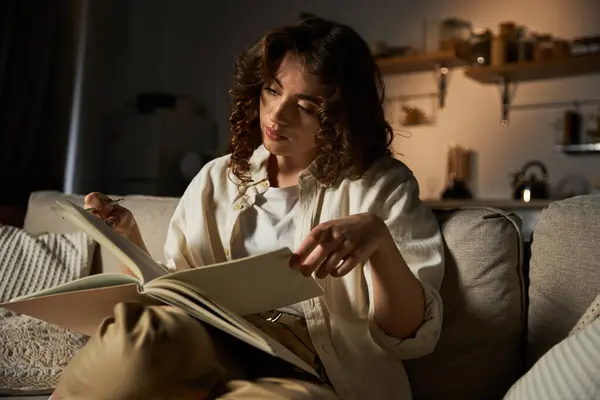 A young woman is comfortably seated at home, immersed in the pages of a captivating book. — Stock Photo