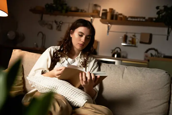 Una bella giovane donna è assorbita in un libro, circondata dal calore della sua casa la sera. — Foto stock