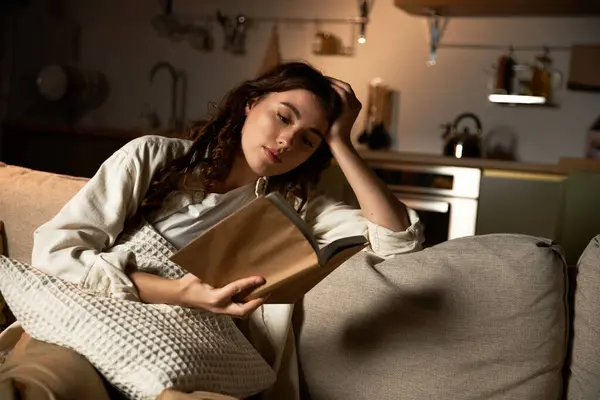 Young woman immerses herself in a book while enjoying the comfort of her cozy living space. — Stock Photo